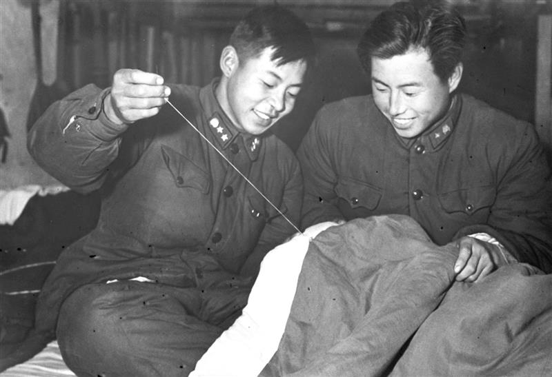 雷锋(左)在帮助战友缝被子。新华社发